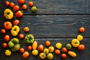 Colorful ripe organic tomatoes on dark rustic table. Fall heirloom. Food background, close up view, flat lay