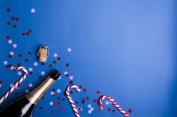 Christmas celebration.Corked bottle of champagne, candy canes, confetti on the blue background