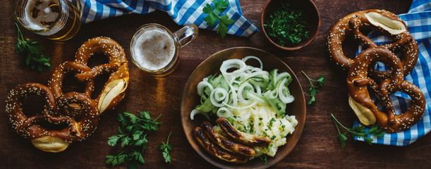 Traditional german appetizer and beer glasses on dark brown wooden table. Mashed potatoes, salad, pretzels and sausages. Oktoberfest party background