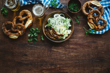 Traditional german appetizer and beer glasses on dark brown wooden table. Mashed potatoes, salad, pretzels and sausages. Oktoberfest party background