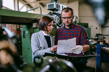Female engineer standing with machinist and analyzing blueprint