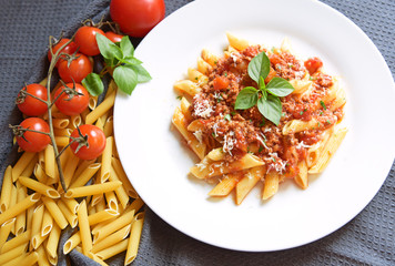 Penne  bolognese with basil leaf on white plate.