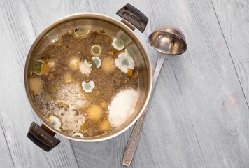 Moldy soup in a pot, poor storage concept, top view on wooden background with copy space.