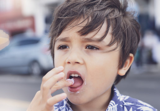 Candid head shot of cute little boy eating condy floss with blurry  street background, Young boy with deep in though while eating  cotton candy, Concept of the international children's day.