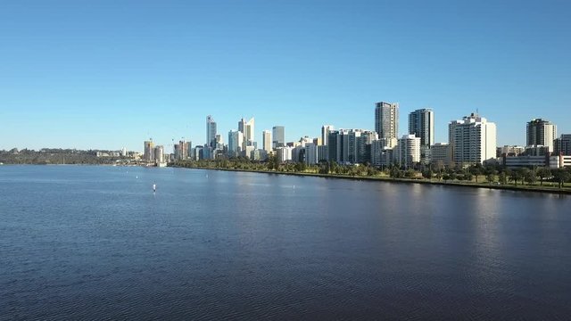 Beautiful scenic aerial view of drone flight above Swan River along the skyline of Perth, capital of Western Australia, with summer sunny blue sky and horizon as background.