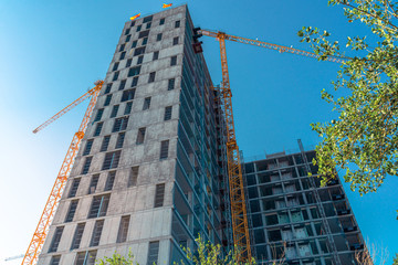 Tall building in construction. Construction site and cranes. Unfinished residential building.