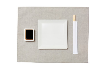 Empty white square plate with chopsticks for sushi and soy sauce on grey napkin background. Top...