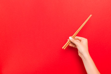 Crop image of female hand holding chopsticks on red background. Japanese food concept with copy space