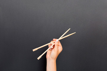 Female hand holding chopsticks on black background. Sushi concept with empty space for your idea