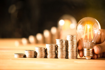 Hand holding a light bulb with coins stack. Creative ideas for saving money concept. Money...