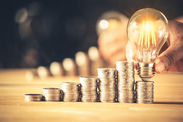 Hand holding a light bulb with coins stack. Creative ideas for saving money concept. Money...