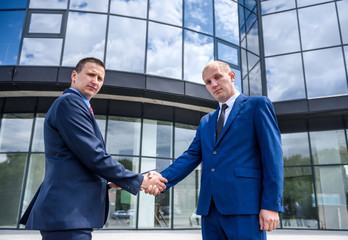 Two businessmen handshaking near skyscraper outdoors