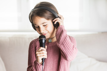 Niña cantando feliz con auriculares y micrófono en interior de casa