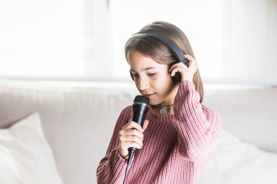 Ni&ntilde;a cantando feliz con auriculares y micr&oacute;fono en interior de casa