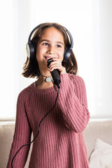 Niña cantando feliz con auriculares y micrófono en interior de casa