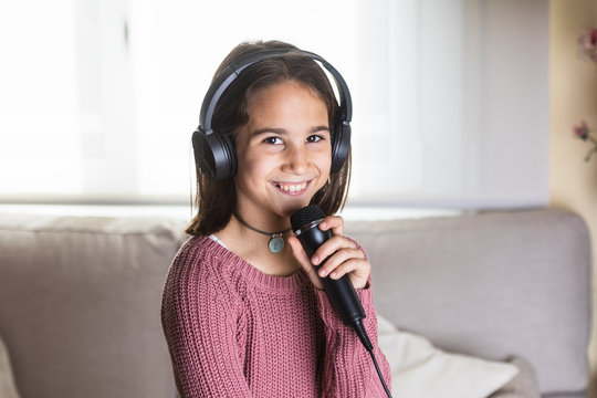 Niña cantando feliz con auriculares y micrófono en interior de casa
