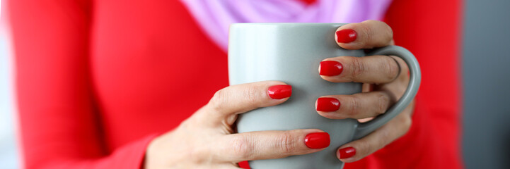 Female hands with red nails holding gray cup of coffee