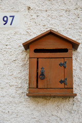 Old wooden mailbox hanging on the wall next to the street number sign.