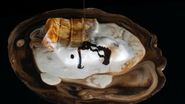 Melting ice cream on which pours chocolate syrup sauce on a black background