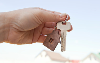 The mental key from door with wooden trinket in shape of house in woman's hand in front of sky