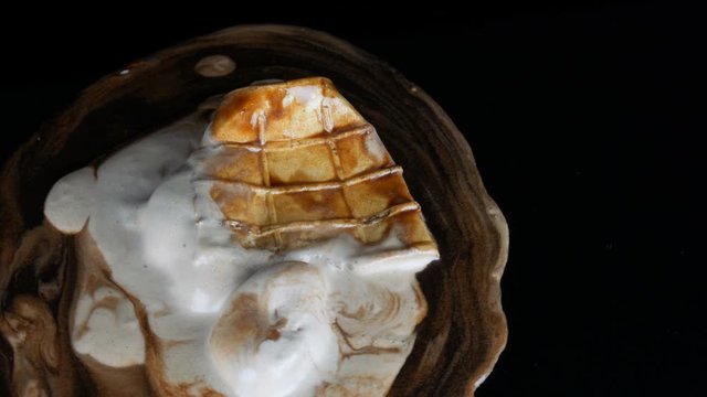 Melting ice cream on which pours chocolate syrup sauce on a black background