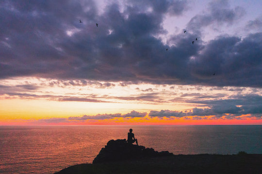 un uomo sulla scogliera al tramonto guarda uccelli, immagine concettuale spirituale