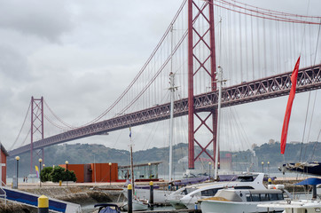 Obraz premium Luxury yachts under the 25 april bridge in Lisbon, Portugal. Port on the Tagus river