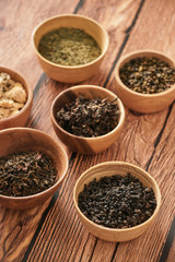 assortment of dry tea in white bowls on wooden surface