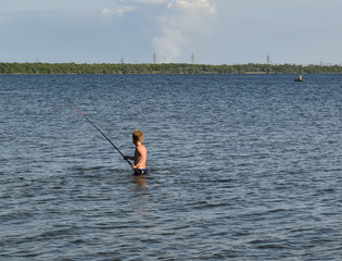 Young boy with a home fishing rod. Fishing in the lake on a summer day. Little fisherman is fishing. Photo of a boy fishing. Boy learns to fish.
