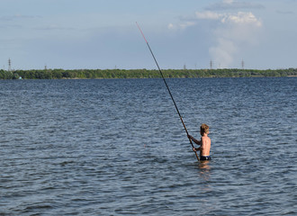Young boy with a home fishing rod. Fishing in the lake on a summer day. Little fisherman is fishing. Boy learns to fish.
