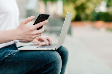 Naklejka premium man using phone and laptop for remote work outdoors