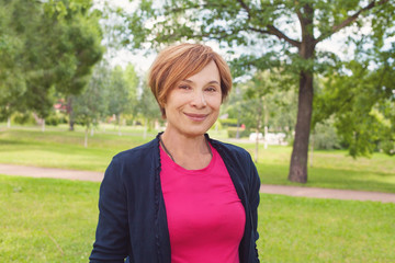 Healthy senior woman walking in park. Older woman with red short haircut outdoors. Mature beauty, 60s