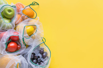 Fruits and summer vegetables in reusable eco friendly mesh bags on bright yellow background. Zero...