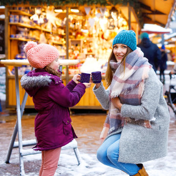 Little cute daughter and mother with cup of steaming hot chocolate or children punch. Happy child girl and beautiful woman on Christmas market in Germany. Traditional leisure for families on xmas.