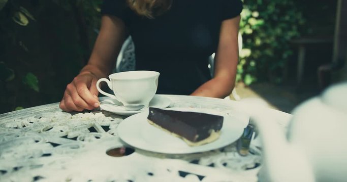 Young woman drinking coffee and eating cake in garden