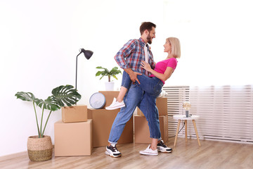 Young married couple wearing casual hipster clothing hugging between many cardboards & things. Husband & wife moving into a new apartment. Boxes & cozy home decorations in empty apartment, Copy space