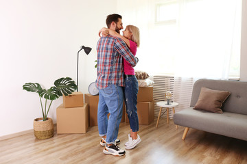 Young married couple wearing casual hipster clothing hugging between many cardboards & things. Husband & wife moving into a new apartment. Boxes & cozy home decorations in empty apartment, Copy space