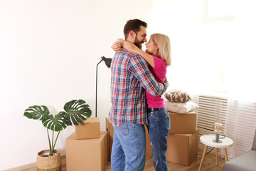 Young married couple wearing casual hipster clothing hugging between many cardboards & things. Husband & wife moving into a new apartment. Boxes & cozy home decorations in empty apartment, Copy space