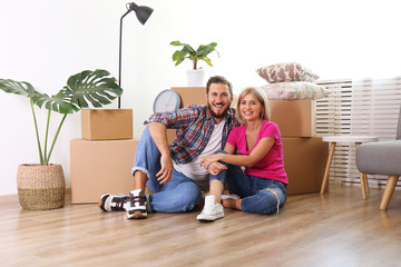 Young married couple moving in new apartment, sitting on the floor between many boxes. New home concept. Bearded man and blonde woman resting after a move-in. Background, copy space, close up.