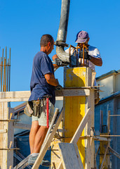 Worker pouring cement pouring into pillars formwork at building area in construction site.