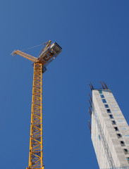 Fototapeta na wymiar a yellow tower crane working on a construction site with a tall concrete building against a bright blue sky