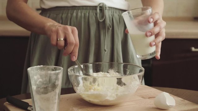 Woman add milk, mixing dough in a glass bowl