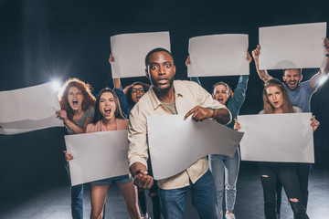 selective focus of shocked african american man near people with blank placards on black