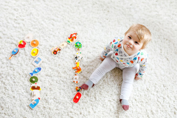 Naklejka premium Gorgeous cute beautiful little baby girl playing with educational toys like wooden puzzle at home or nursery. Happy healthy child having fun with colorful different toys. Kid learning different skills