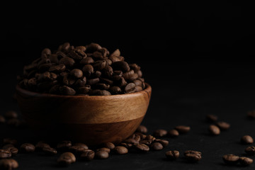 roasted coffee beans in wood bowl on black background. close up