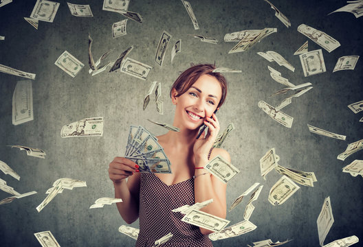 attractive woman talking on a smartphone holding money, cashback under dollar rain