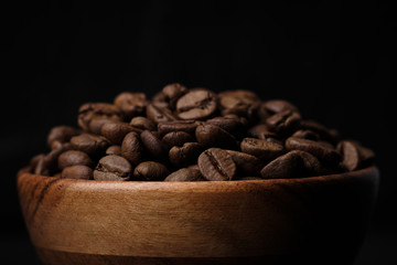 roasted coffee beans in wood bowl on black background. close up