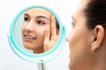 Attractive young woman with hand mirror touching crow's feet.