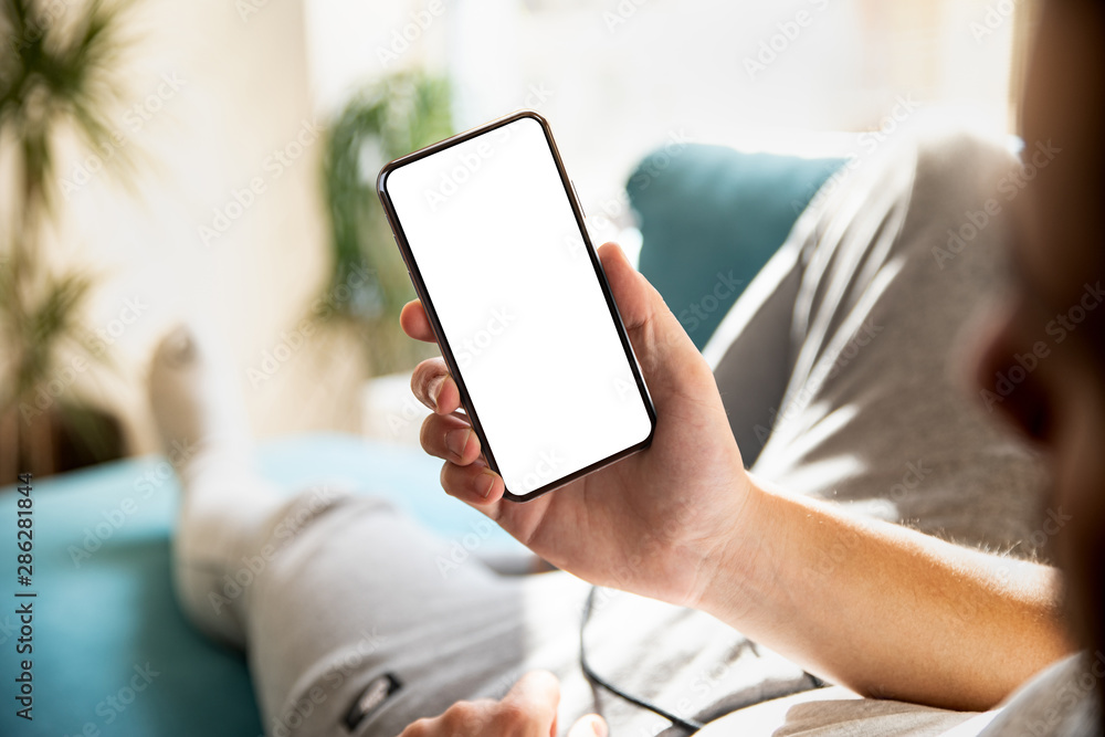 Poster man using smartphone blank screen frameless modern design while lying on the sofa in home interior