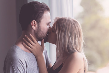 Couple hugging together. White youngman and woman standing near window with autum leafs in background. Holding and kissing her husband. With light leaks.